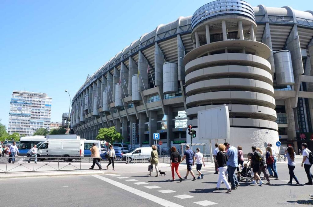 Fachada do Estádio Santiago Bernabéu com torre espiral e pedestres atravessando a rua.