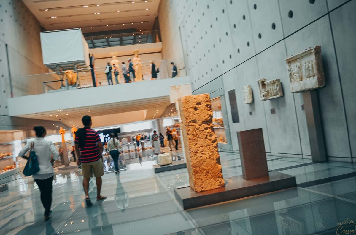 galeria-rampa-achados-museu-acropole-atenas Visitantes caminhando pelo piso de vidro inclinado da galeria principal no Museu da Acrópole.