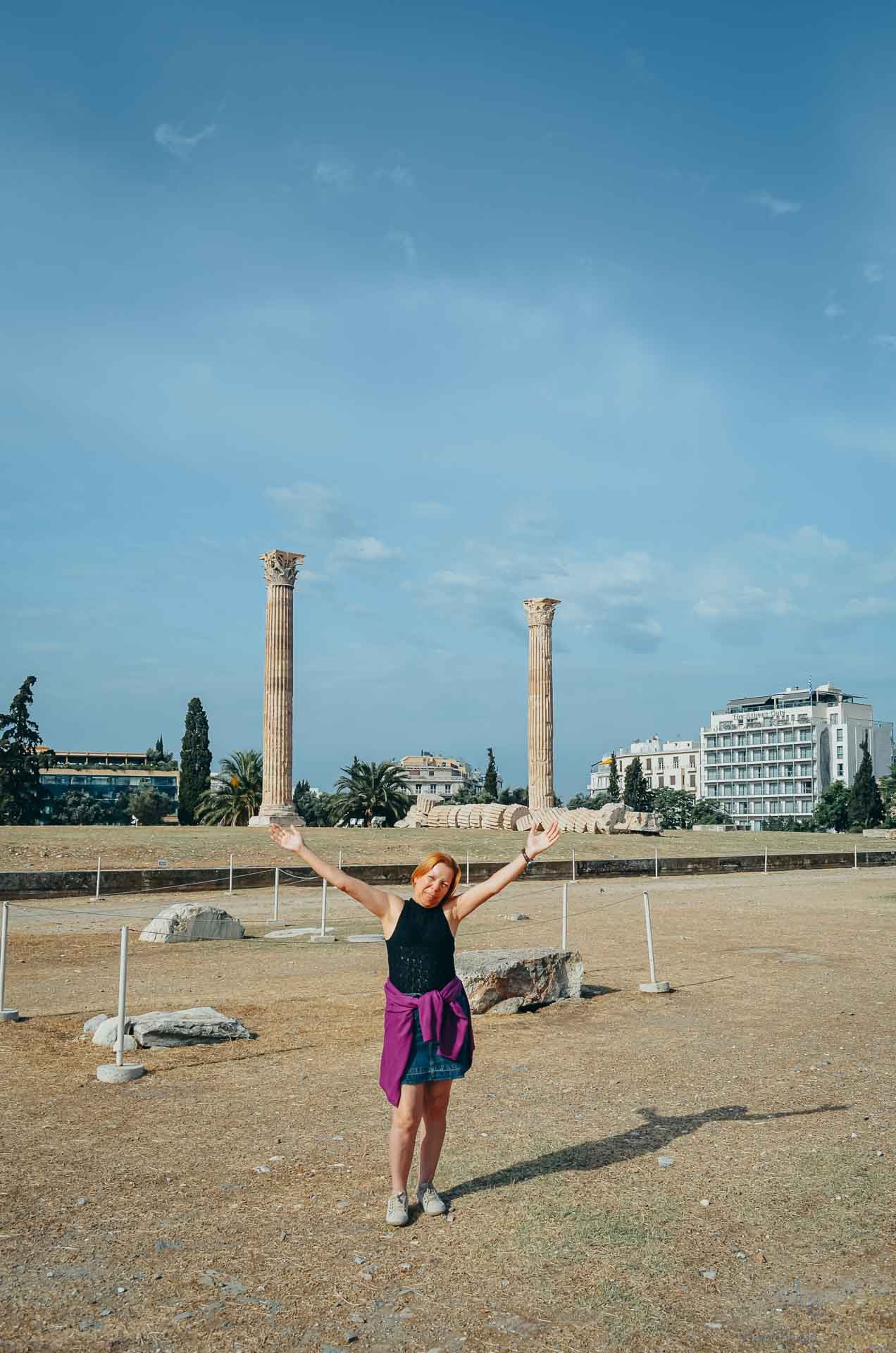 mulher-bracos-abertos-templo-zeus-atenas Mulher de braços abertos sorrindo no sítio arqueológico do Templo de Zeus Olímpico em Atenas.