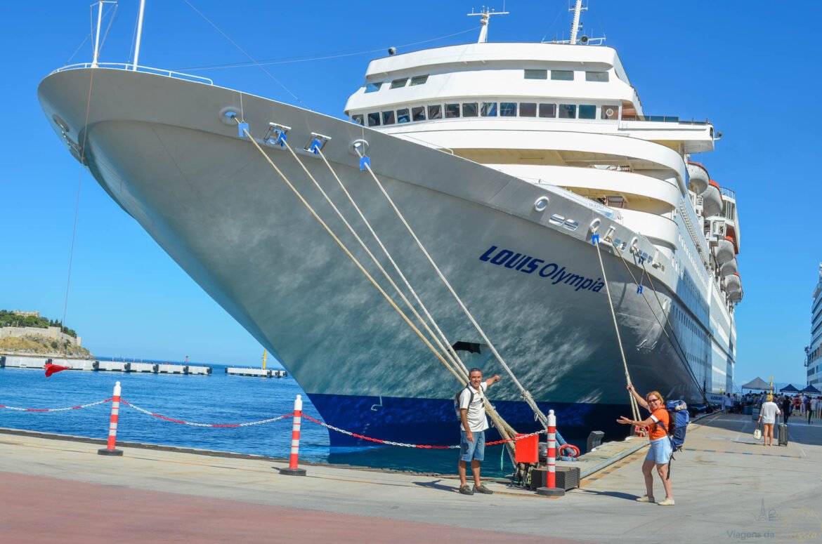 Navio de cruzeiro Louis Olympia atracado no porto com casal segurando cabos de amarração.