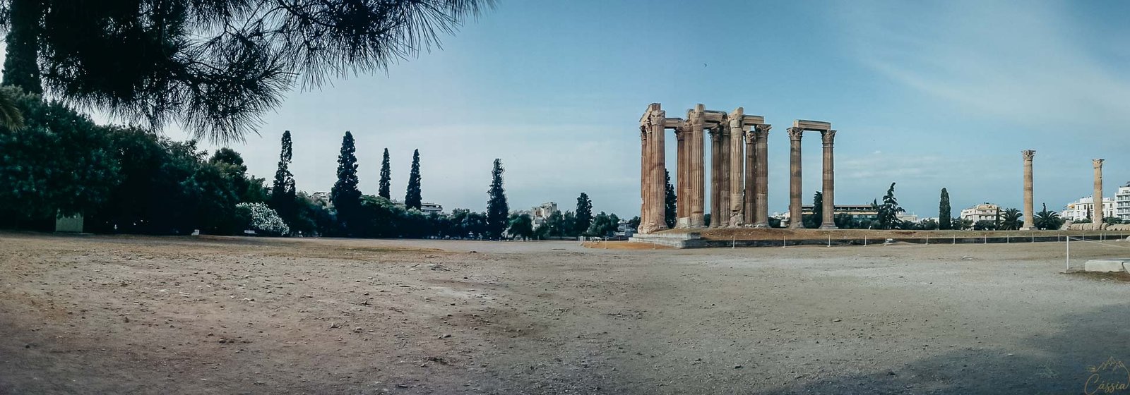panoramica-templo-zeus-olimpico-atenas Vista ampla e panorâmica do sítio arqueológico do Templo de Zeus Olímpico com céu azul.