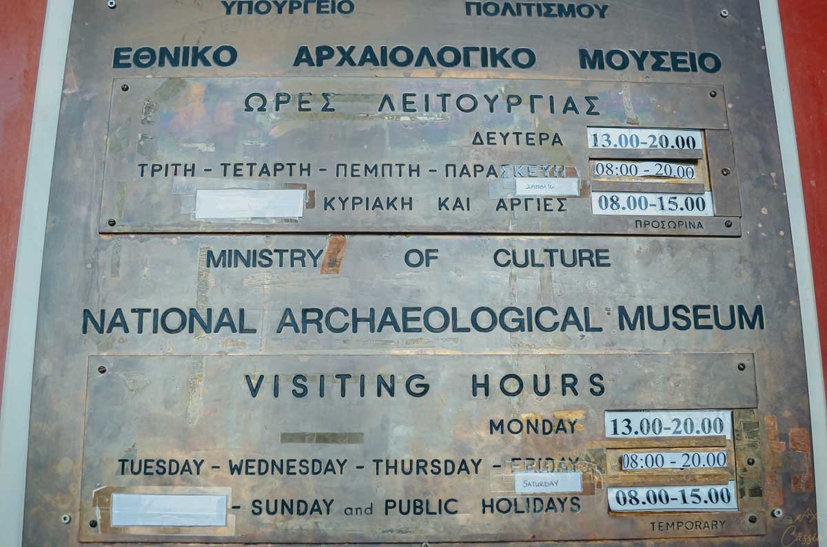 placa-horario-museu-arqueologico-nacional-atenas Placa informativa de metal com horários de funcionamento do Museu Arqueológico Nacional em grego e inglês.
