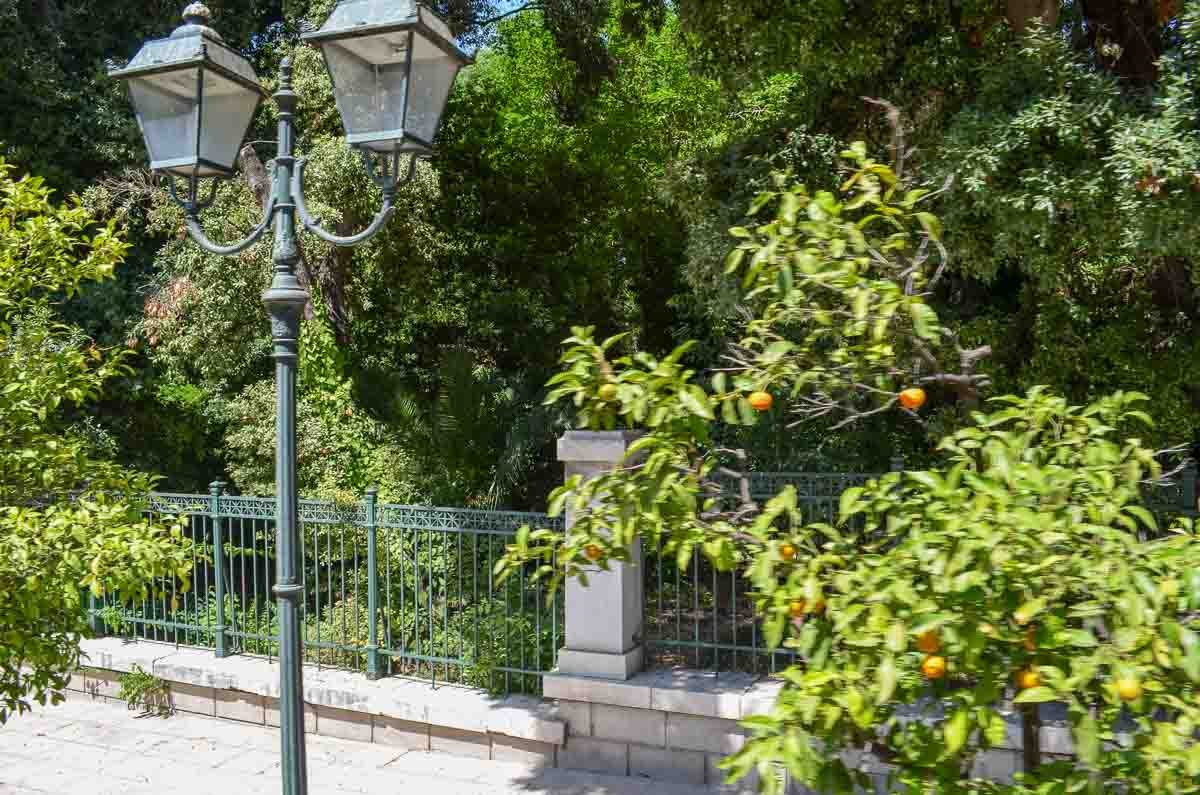 poste-iluminação-antigo-jardim-atenas-grécia Poste de iluminação estilo antigo cercado por laranjeiras e gradil de ferro.