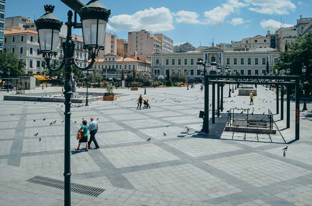 praça-kotzia-prefeitura-atenas-grécia Vista ampla da Praça Kotzia pavimentada com pombos e edifícios neoclássicos em Atenas.