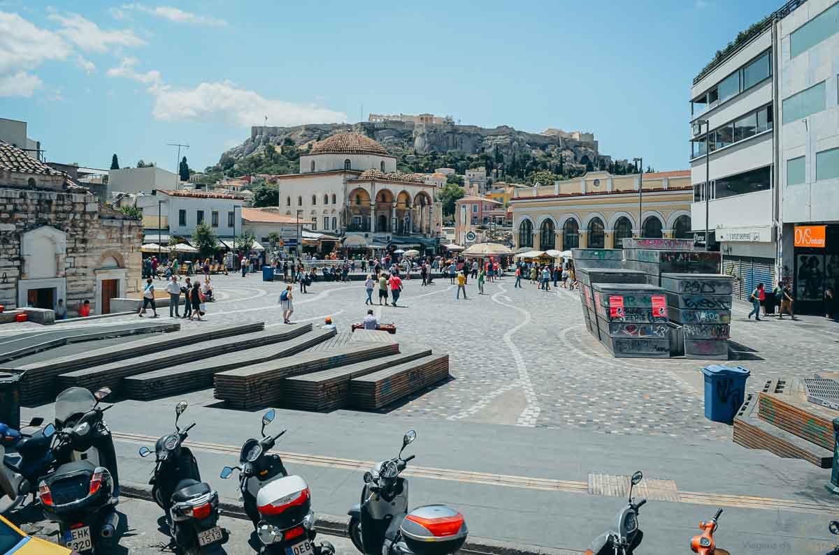 praça-monastiraki-acrópole-atenas-grécia Praça Monastiraki ampla em Atenas com a Acrópole histórica visível ao fundo sob céu claro.