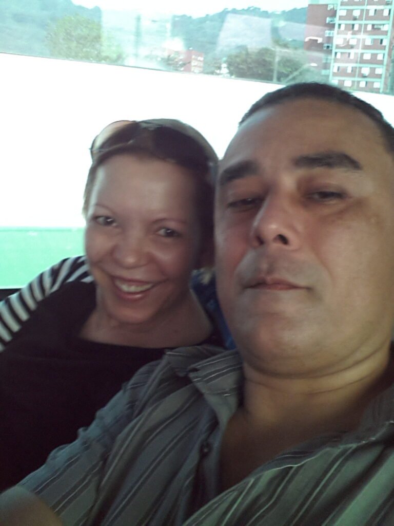 Selfie em close de um casal sorrindo em ambiente interno iluminado.