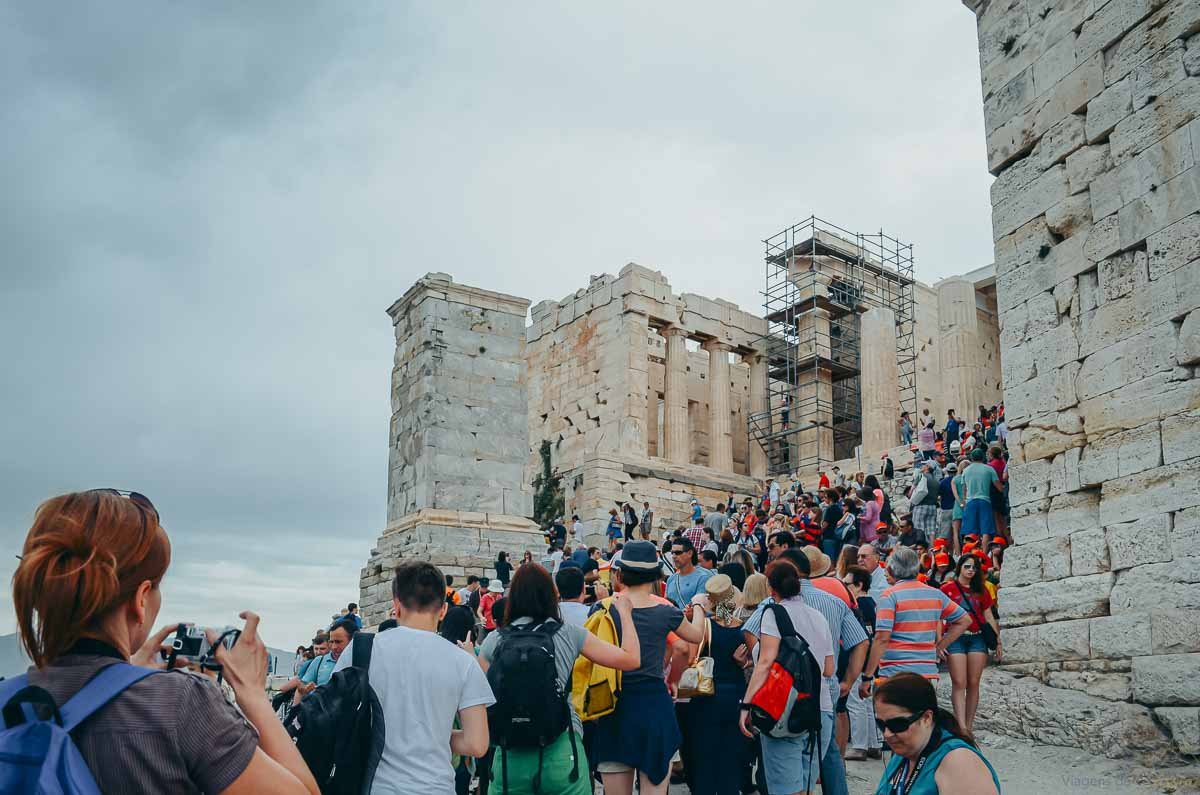 subida-propileus-portao-entrada-acropole-atenas Turistas subindo a rampa de acesso entre as colunas e blocos dos Propileus na Acrópole.