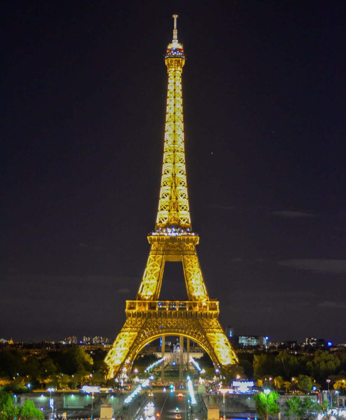 Torre Eiffel totalmente iluminada em tons dourados contra o céu escuro da noite em Paris.