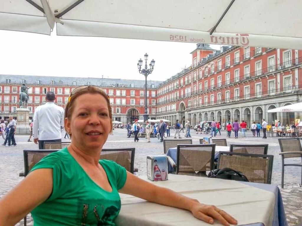 Mulher de camiseta verde sentada à mesa de café ao ar livre na Plaza Mayor de Madri.