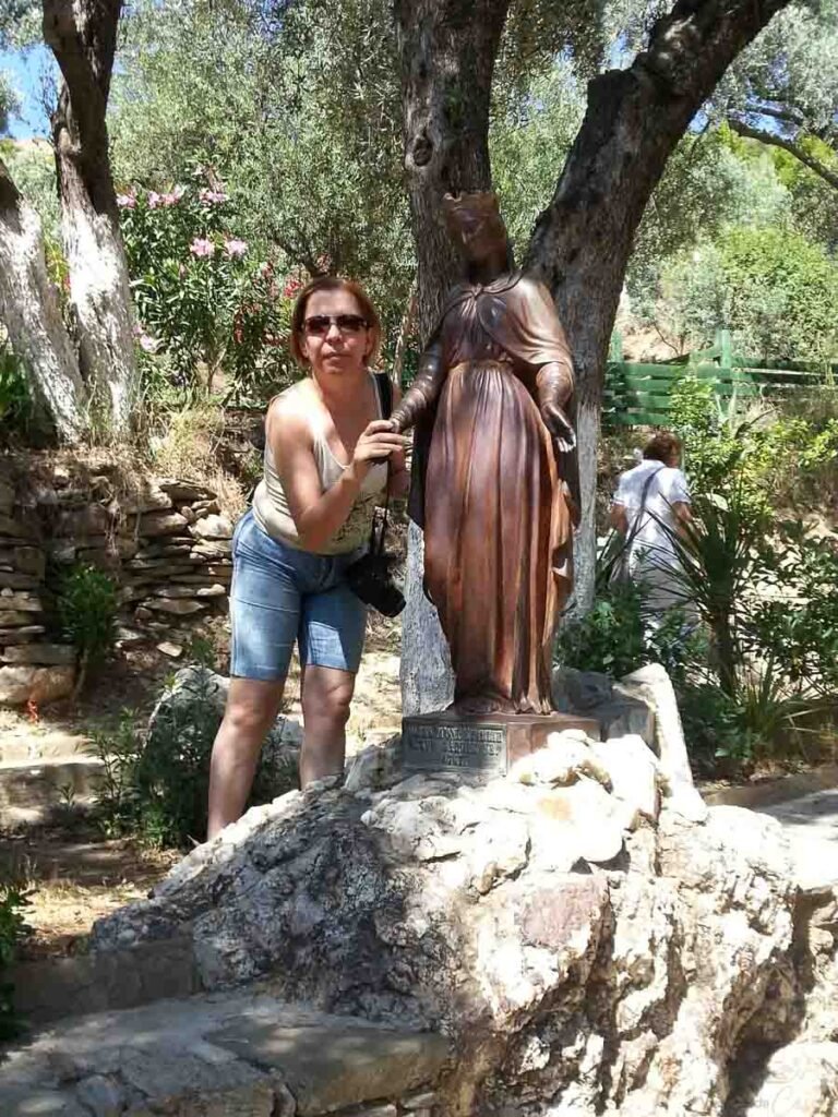 Mulher posando suavemente ao lado da estátua de bronze da Virgem Maria no santuário.