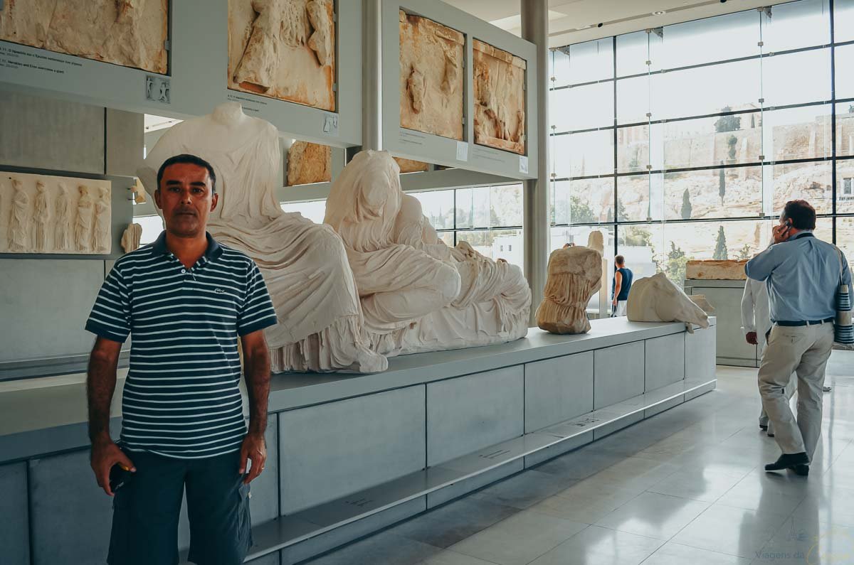 visitante-galeria-partenon-museu-acropole Homem de camisa polo listrada diante de esculturas e relevos de mármore no Museu da Acrópole.